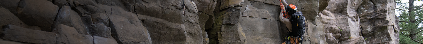 female hiker climbing up the rock wall with their Alpinisto pack.